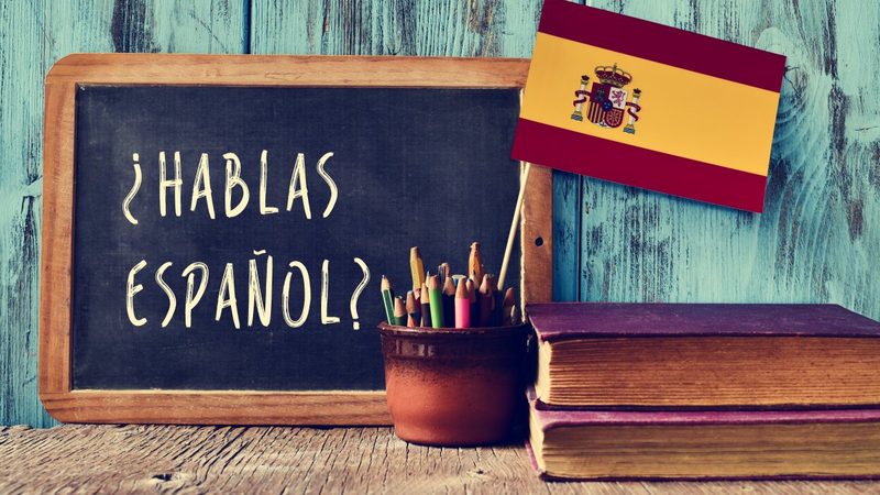 Een schoolbord met de vraag « ¿Hablas español ? » naast de Spaanse vlag.
